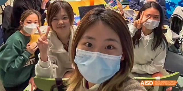 A female student wearing a face mask and making a peace sign while taking a selfie at Beijing International Bilingual Academy.