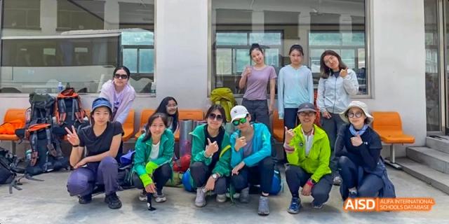 A group of adults and students in casual clothing kneeling and posing for a group photo outdoors at Beijing International Bilingual Academy.