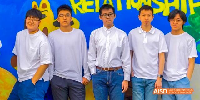 Four individuals standing together, wearing white shirts and blue jeans, at Beijing International Bilingual Academy.