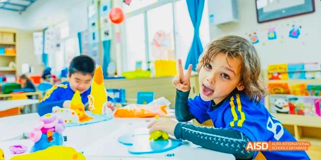 A young boy and a girl with a big smile and curly hair sitting at a desk in a classroom at Beijing International Bilingual Academy.