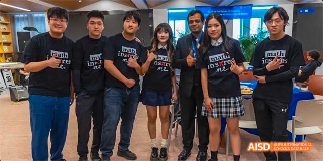 A group of students and adults in black t-shirts with a team logo posing for a photo at Beijing International Bilingual Academy.