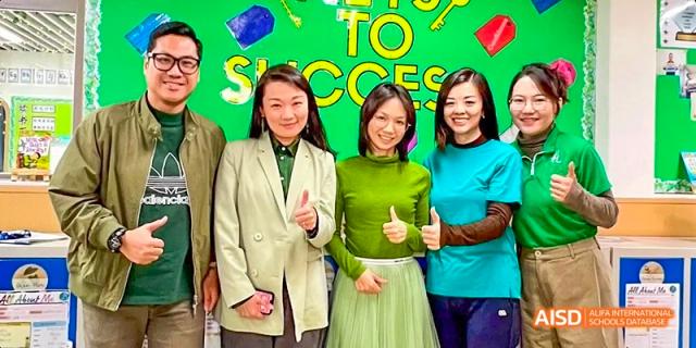 A group of people, some wearing green outfits, posing for a photo with a thumbs-up at Beijing International Bilingual Academy.