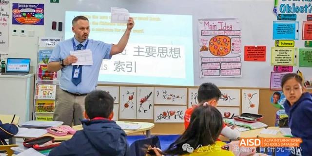 A teacher pointing to a whiteboard with Chinese characters on it, while surrounded by students at Beijing International Bilingual Academy.