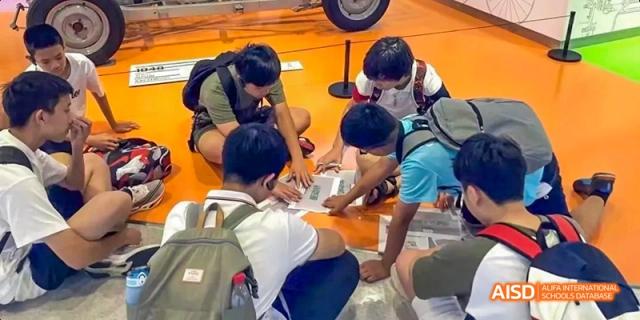 Students and a teacher collaborating on a project, gathered around a table with various materials at Beijing International Bilingual Academy.