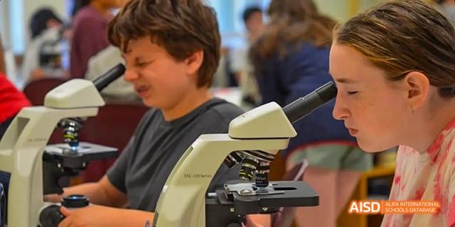 Two students looking into a microscope in a classroom at Beijing International Bilingual Academy.