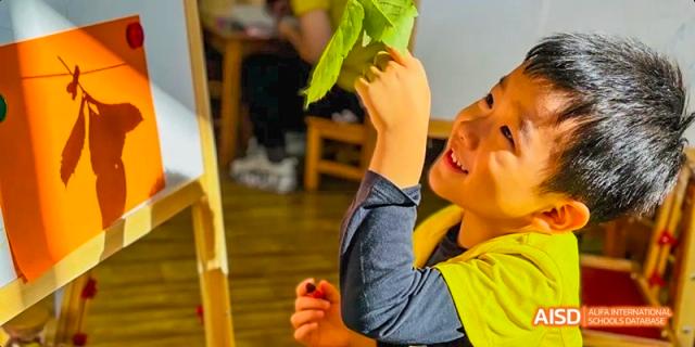 A young student smiling while holding up a plant or leaf at Beijing International Bilingual Academy.