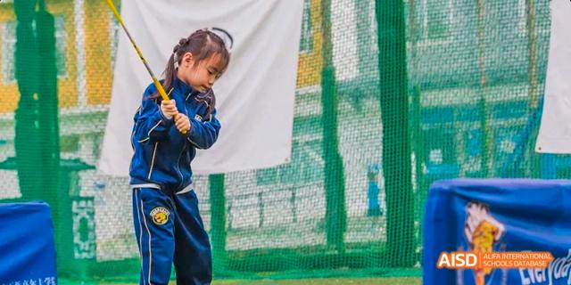 A female student in a blue jacket holding a baseball bat and smiling at Beijing International Bilingual Academy.