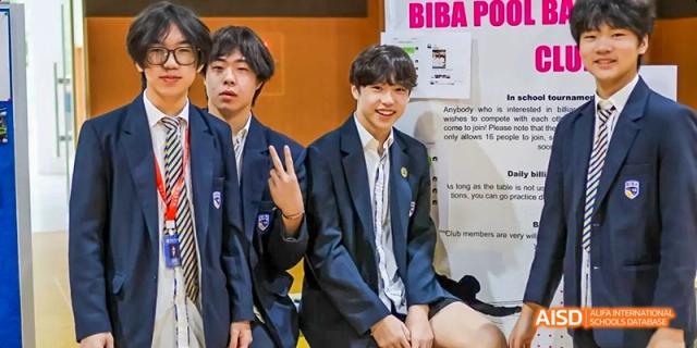 Two male students in formal uniforms, one holding a piece of paper at Beijing International Bilingual Academy.