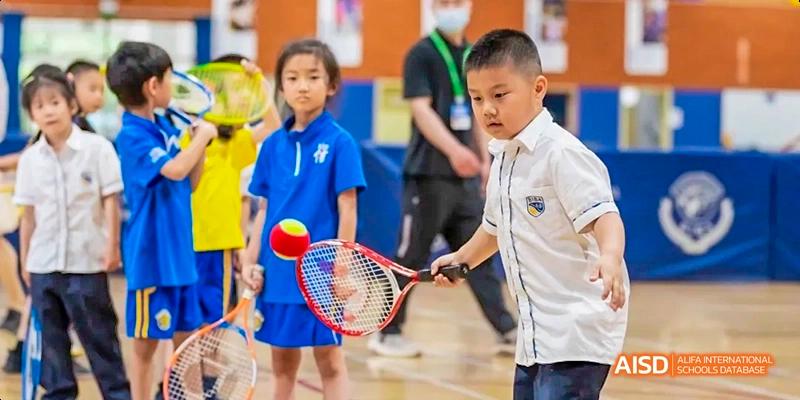 A young male student in a white polo shirt playing tennis indoors at Beijing International Bilingual Academy.