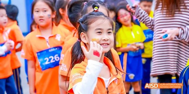 A young female student wearing an orange jacket and smiling during a sports event at Beijing International Bilingual Academy.