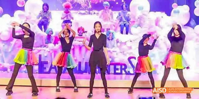 A group of young female students in black and colorful outfits performing a dance on stage at Beijing International Bilingual Academy.
