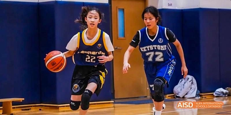 Two female students playing basketball in a gymnasium at Beijing International Bilingual Academy.