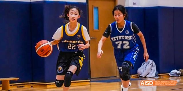 Two female students playing basketball in a gymnasium at Beijing International Bilingual Academy.