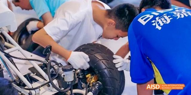 A male student working on a motorcycle tire with an adult at Beijing International Bilingual Academy.
