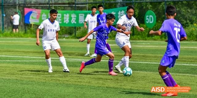 Two teams of students playing a soccer match on a green field at Beijing International Bilingual Academy.