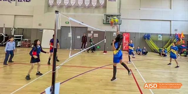A female student playing volleyball, with the net in the foreground at Beijing International Bilingual Academy.
