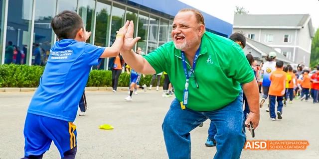 A male student giving a high-five to a man in a green shirt during a sports event at Beijing International Bilingual Academy.