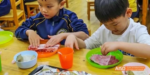 Two young students are focused on a cooking activity, with hands-on food preparation at Beijing International Bilingual Academy.