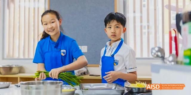 A young female and male student are smiling while preparing vegetables in a kitchen setting at Beijing International Bilingual Academy.