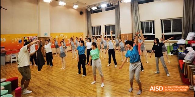 A group of students and adults from Beijing National Day School International Department participating in an exercise or dance class indoors.