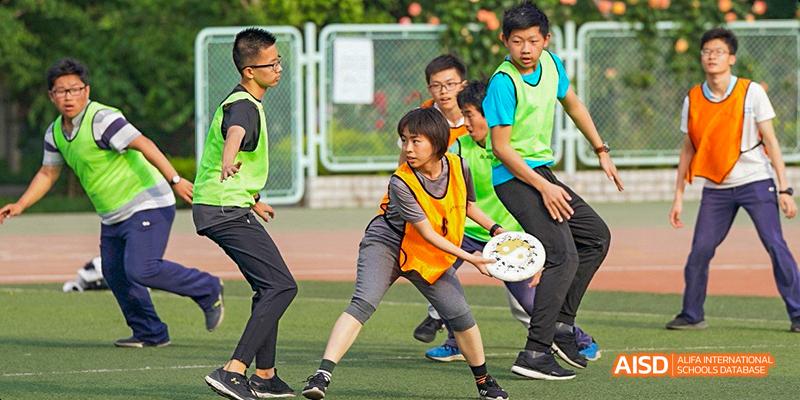 Students from Beijing National Day School International Department playing a field sport, possibly Ultimate Frisbee, outdoors.