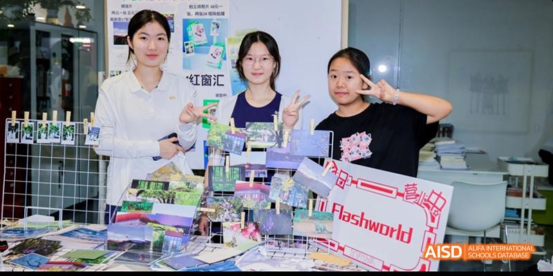 Students and a teacher from Beijing National Day School International Department smiling and posing with school projects at a table.