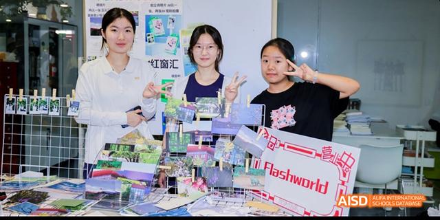 Students and a teacher from Beijing National Day School International Department smiling and posing with school projects at a table.