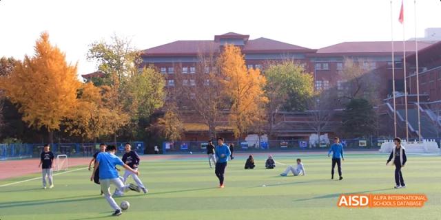 Students from Beijing National Day School International Department playing soccer on a field during a sunny autumn day.