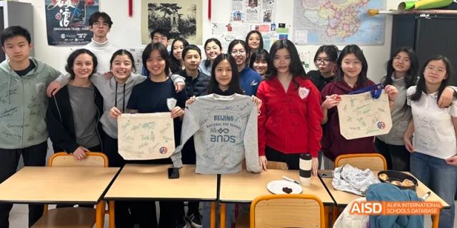 Students from Beijing National Day School International Department holding up t-shirts they designed in a classroom.