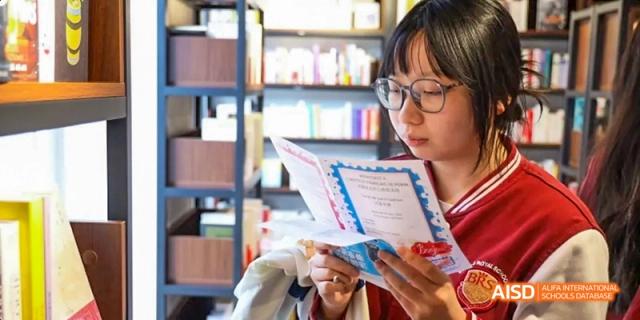 A photo showing a female student standing in a library, at Beijing Royal School.