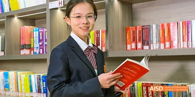 A photo showing a male teacher holding a book in a library, at Beijing Royal School.