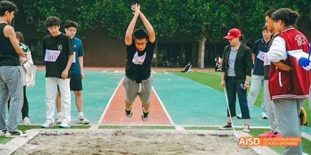 A photo showing a student doing a long jump, at Beijing Royal School.