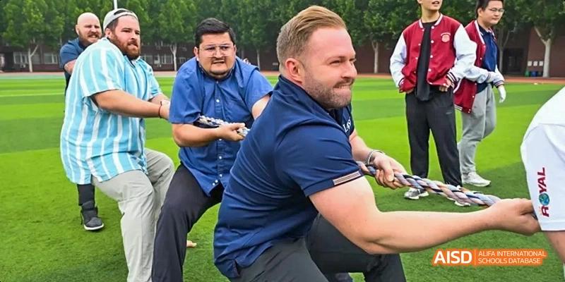 A photo showing two male teachers on a field, one pulling a rope, at Beijing Royal School.