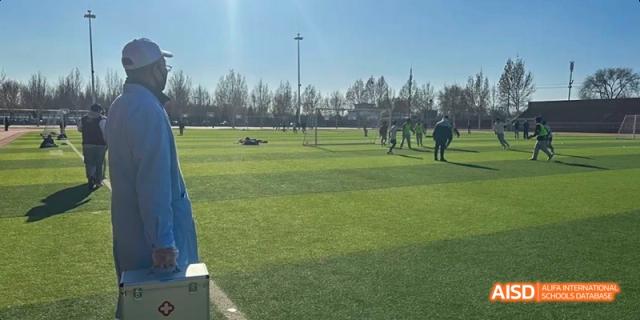 A photo showing students playing football on a field, at Beijing Royal School.