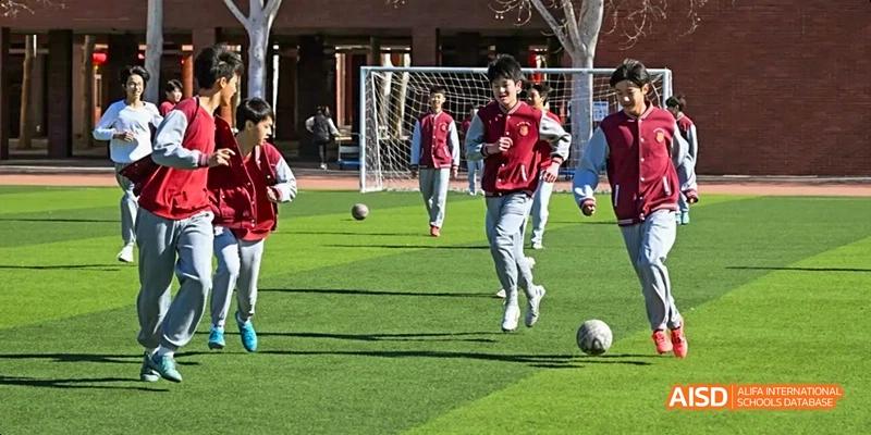 A photo showing students playing football on a field, at Beijing Royal School.