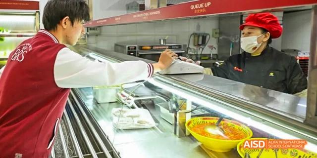 A photo showing a student getting food in a cafeteria, at Beijing Royal School.