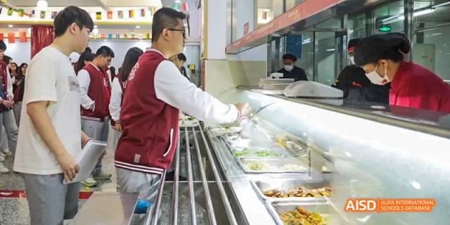 A photo showing a man in a cafeteria giving food to a student, at Beijing Royal School.