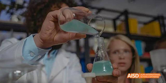 A female student from Beilu Academy, holding a cup and looking at a science experiment.