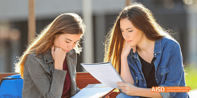 Two female students from Beilu Academy, studying together with a book and papers on a table.