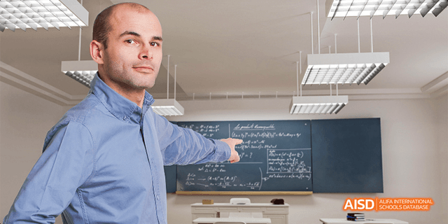 A male teacher from Beilu Academy, pointing at a blackboard in a classroom.
