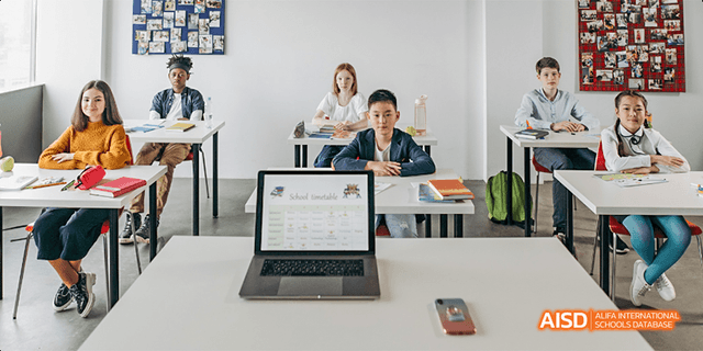 A female and a male student from Beilu Academy, sitting at desks and looking at a laptop computer.