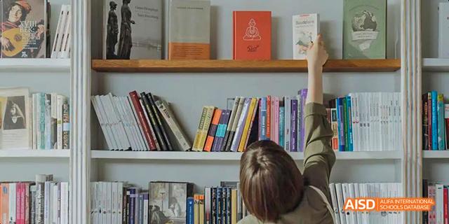 A student from Beilu Academy, raising their hand in a classroom with bookshelves in the background.