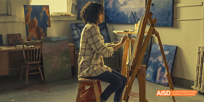 A student from Beilu Academy, sitting at an easel and painting on a canvas in an art studio.