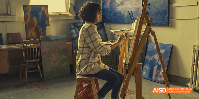 A student from Beilu Academy, sitting at an easel and painting on a canvas in an art studio.