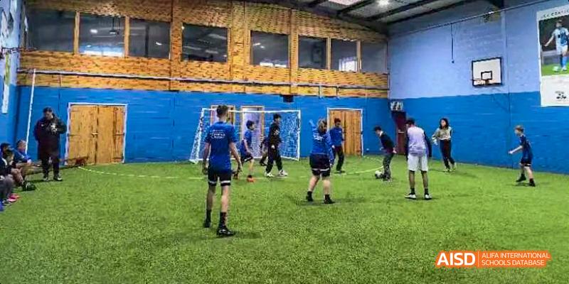 A group of students from Beilu Academy, wearing blue uniforms, playing soccer on an indoor turf field.
