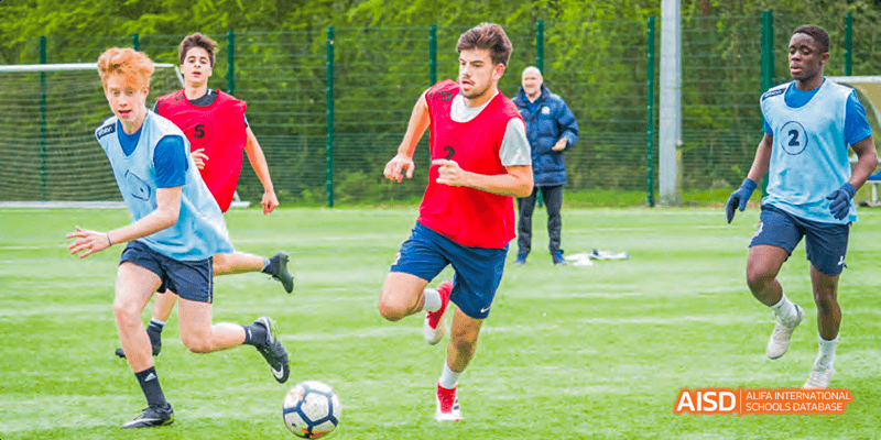 A student from Beilu Academy, kicking a soccer ball on a green field during a game.