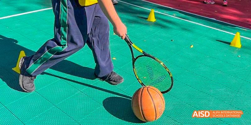 A close-up view of a student from Beilu Academy, holding a tennis racket next to a basketball on a court.