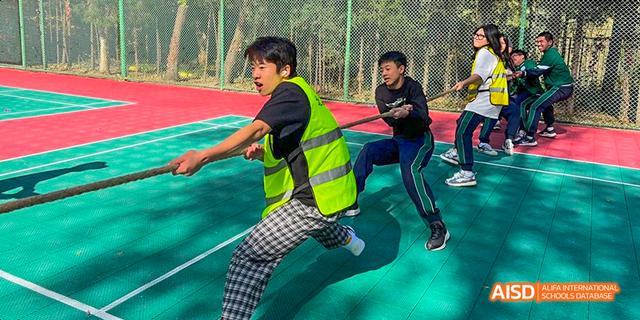 A student from Beilu Academy, wearing a bright yellow vest, jumping over an obstacle during a sports activity.