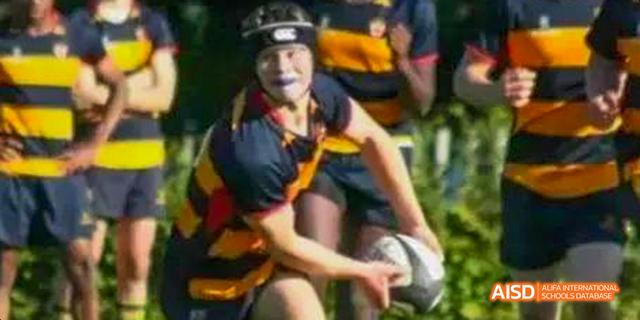 A student from Beilu Academy, in a yellow and black jersey, holding a rugby ball during a match.