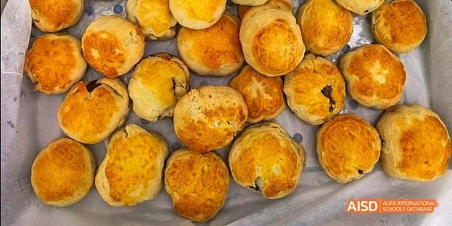 A pile of round, golden-brown baked goods, possibly scones or buns, representing food served at Beilu Academy.